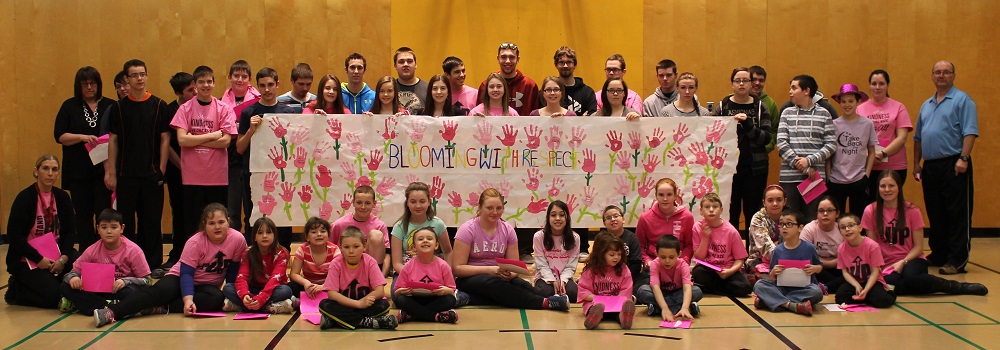Students and staff pose with the beautiful Blooming with Respect banner created on this year's Pink shirt Day - a collaborative effort showcasing everyone's handprints and thoughts about what respect means to them. (Photo credit: Bonita Rumbolt)